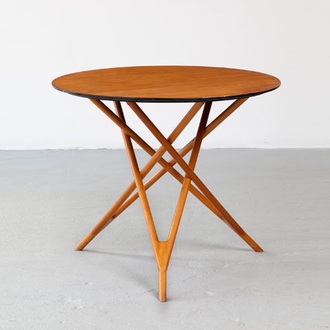 A small rich stained coffee table with a round tabletop and legs that interweave in a creative way
