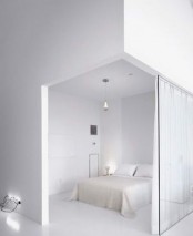 a crispy white minimalist bedroom with a white bed and bedding, pendant and table lamps and a glass space divider with curtains