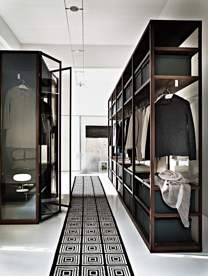 A minimalist closet done with dark stained wooden shelves, a glass armoire and a graphic rug