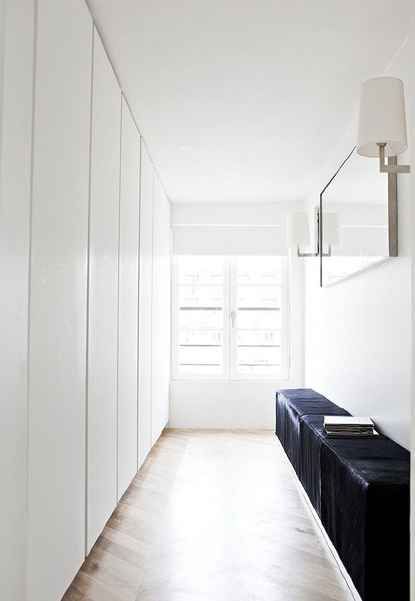 An ultra minimalist closet with lots of wardrobes done in white, with sleek panels and a black leather bench