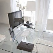 a sophisticated minimalist home office with a clear glass desk, a white chair, a floor lamp and some gadgets is an ultimate workspace