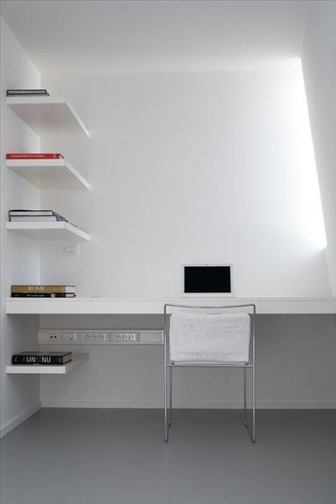 A minimalist white home office with a skylight, a built in desk and matching shelves plus a white chair is a cool space to work