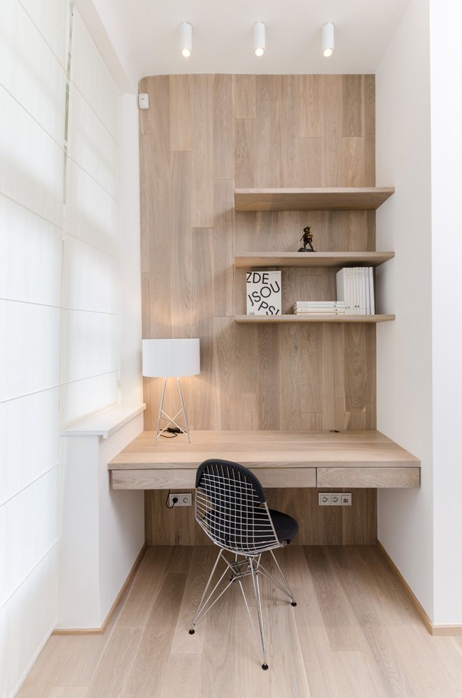 A minimalist home office nook clad with wood, with several shelves, a built in desk and a black chair plus some lights for comfortable working