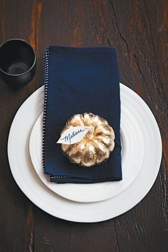 A modern place setting with white plates, a navy napkin, a gilded pumpkin with a tag
