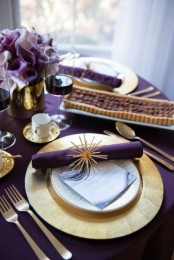 a modern Thanksgiving tablescape done in purple and gold with chic floral arrangements and elegant gold charger and cutlery