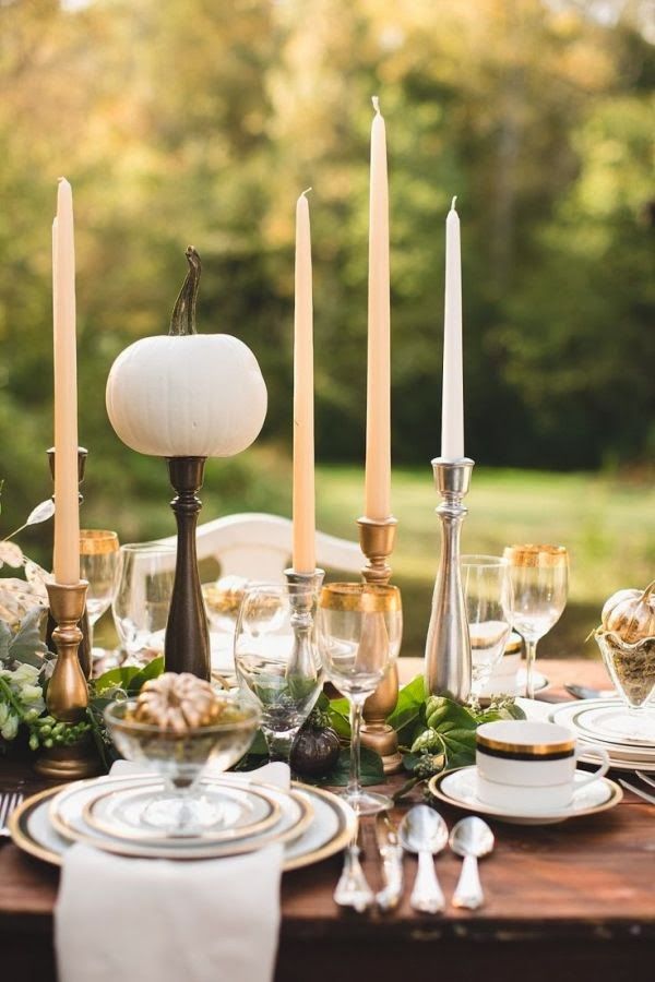 a modern refined Thanksgiving tablescape with thin and tall candles, a greeneyr runner and fresh pumpkins