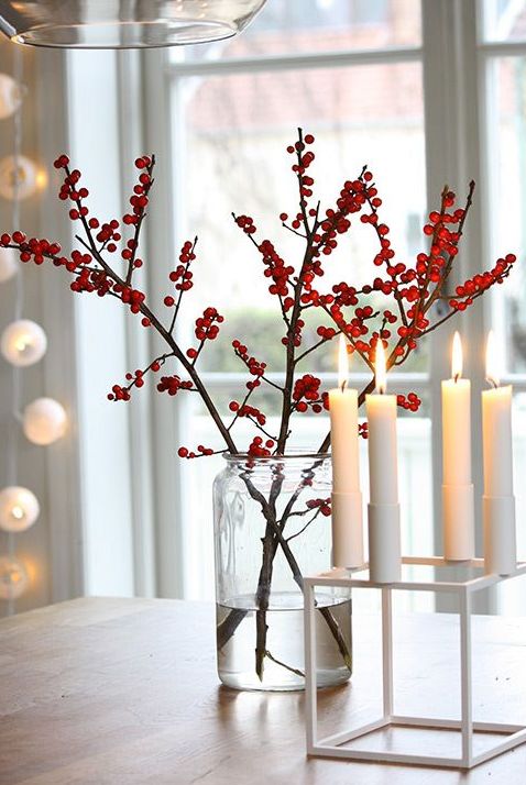 a red berry arrangement in a clear vase and some candles in a modern white candleholder for simple modern decor