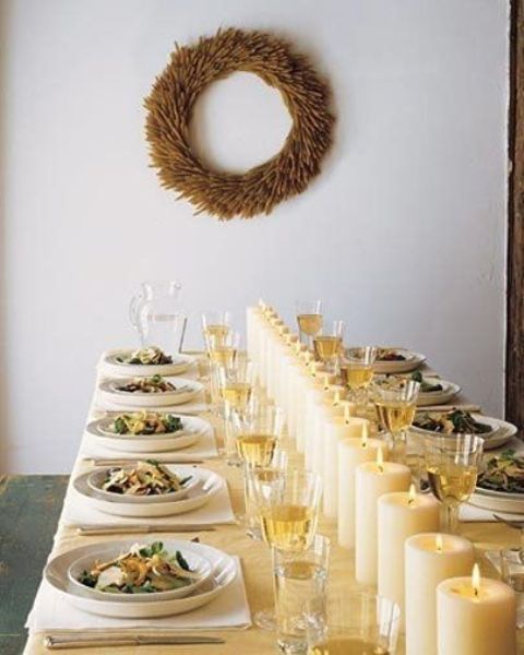 a modern table setting with a row of pillar candles instead of a table runner or centerpiece and a wreath on the wall