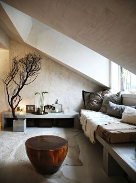 A neutral wabi sabi living room with an attic ceiling and a window, concrete benches, a tree stump side table and some branches for decor