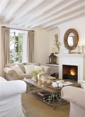 a neutral French farmhouse living room with whitewashed wooden beams, a fireplace, neutral seating furniture and a refined coffee table in the center