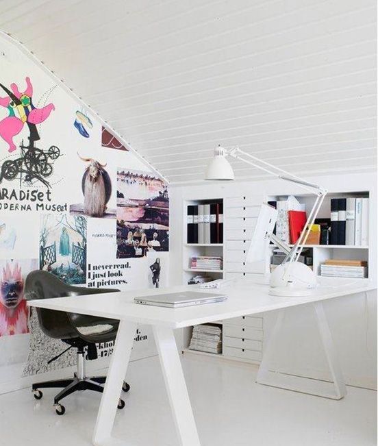 A cool Nordic home office done in white, with built in shelves and drawers, a trestle desk, a black chair and an accent wall with lots of fun art and decor