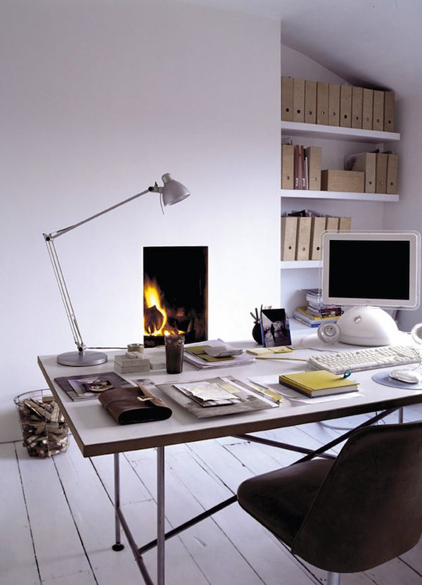 A white Nordic home office with lots of built in bookshelves, a fireplace, a large desk and a black chair, a silver table lamp is a beautiful space