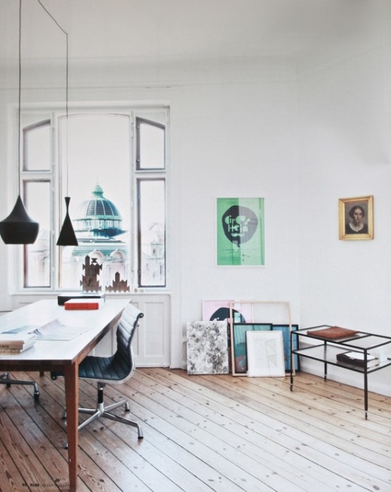 an airy Scandinavian home office with a large desk, a black chair, black pendant lamps and a black storage unit and artwork