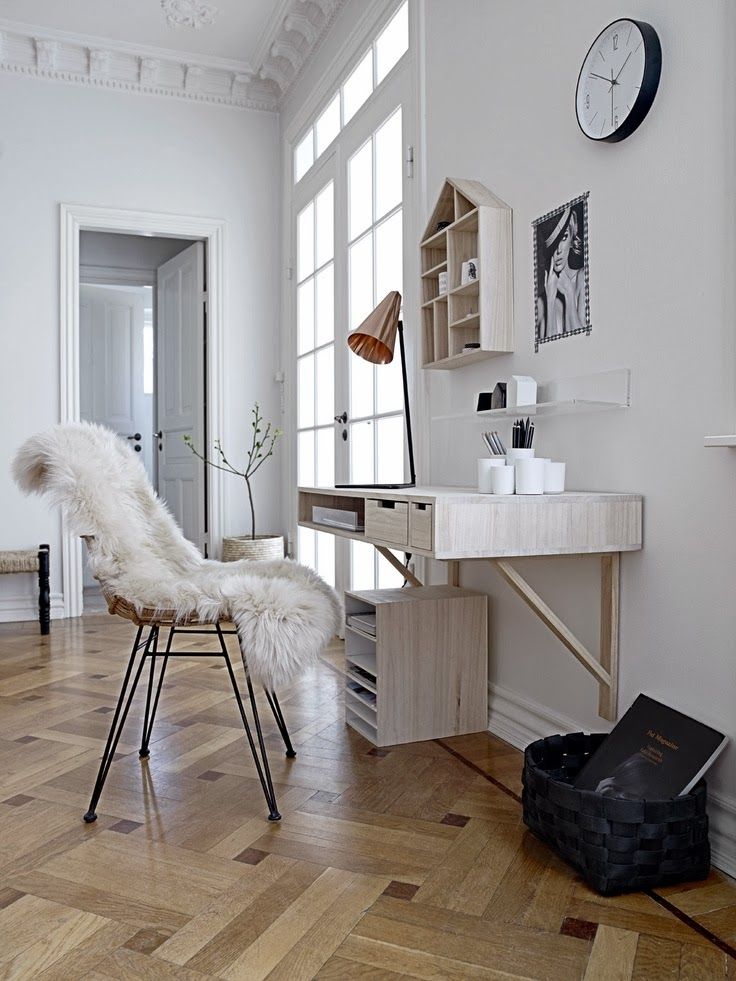 A Nordic white home office with a wall mounted desk, a cabinets for storage, a house shaped wall mounted shelf and a cane chair