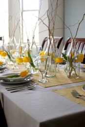an off-white tablecloth, yellow printed placemats, yellow tulips and branches for centerpieces