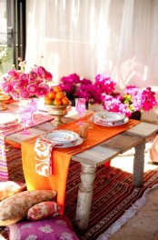 a super bright and colorful table setting in Moroccan style, with pink blooms, colorful napkins and runners and bright pillows