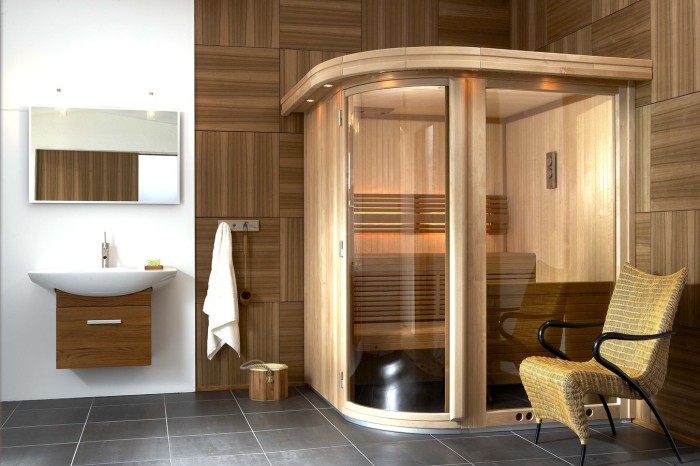 A tiny steam room clad with wood and glass, with a single wooden bench and some built in lights