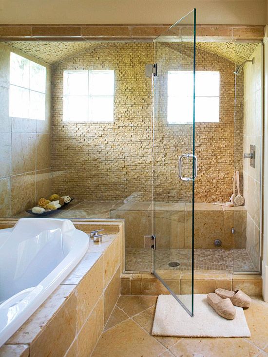 a light-filled steam room clad with stone and matching tiles, with a large bench and some bowls with shower poufs and foams