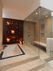 a large neutral steam room with various neutral tiles on the floor and walls, built-in shelves and a bench plus built-in lights and glass walls