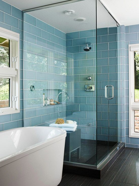 A small steam room with blue and black tiles, with a built in niche for storage and a bench of wood