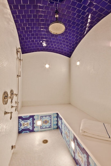 a bold steam room clad with purple and white tiles, with a large tile clad bench and some patterns all over the bench