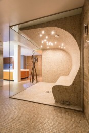 a stylish neutral steam room clad with small scale tiles, with a single bench that appers curved  from the wall