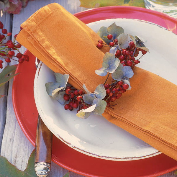 Layered white and red plates paired with an orange napkin with a berry and leaf napkin ring is a very stylish solution for a modern Thanksgiving place setting