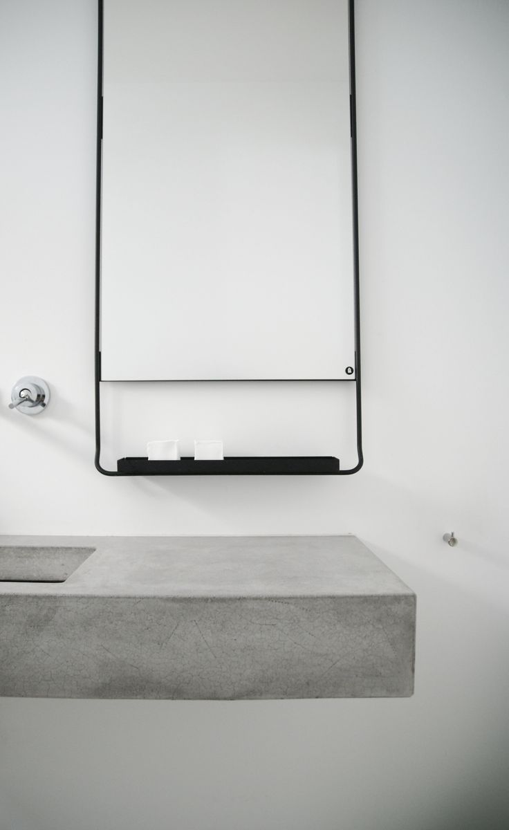 A floating concrete vanity with a sink, a black metal shelf with soaps for an ultra minimalist bathroom