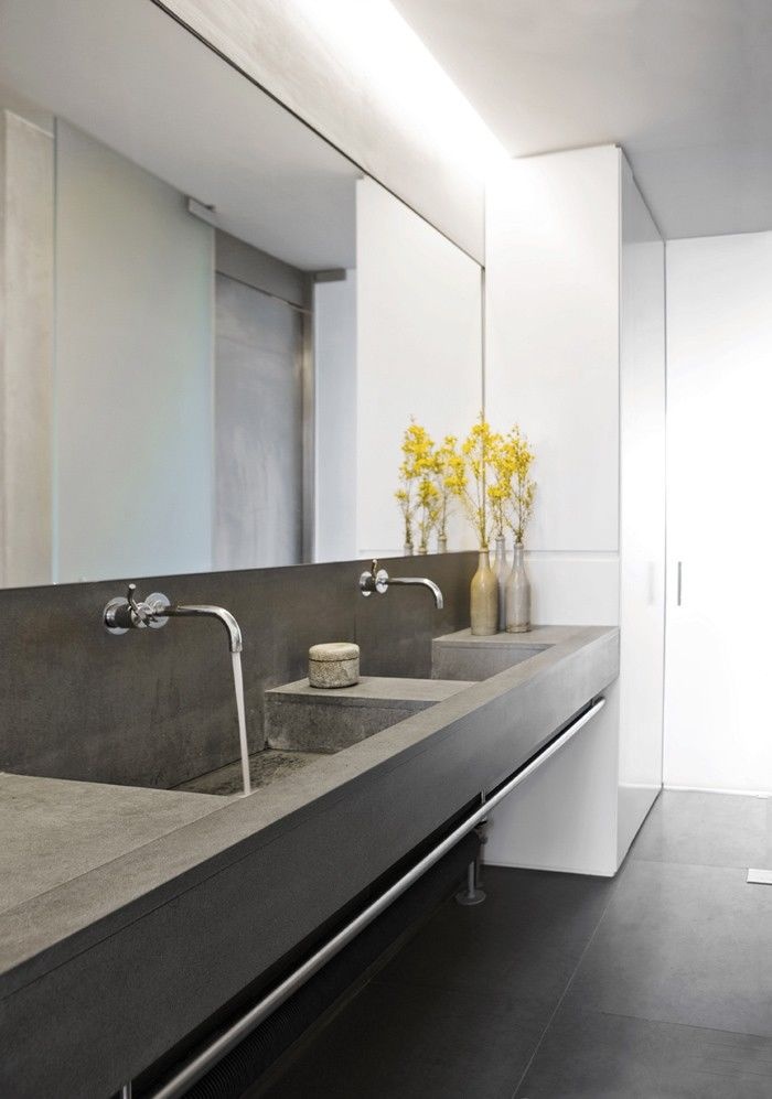 A minimalist bathroom with a double concrete vanity with built in sinks, a large mirror and a mirror wardrobe right here