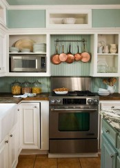 a cozy mint-colored and white cottage kitchen with open and closed storage units, a metal cooker and copper pans for decor is a very stylish space