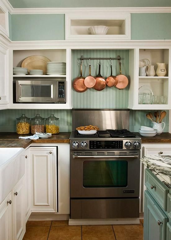 A cozy mint colored and white cottage kitchen with open and closed storage units, a metal cooker and copper pans for decor is a very stylish space