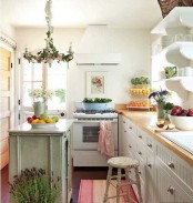 a neutral cottage kitchen with white beadboard cabinets with butcherblock countertops, a shabby chic green kitchen island, a greenery woven chandelier and floral artworks