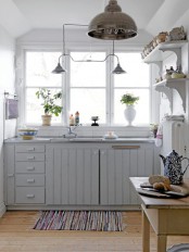 a light grey kitchen with planked cabinets, vintage lamps and vintage shelves, printed textiles and potted plants