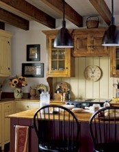 a neutral cottage kitchen with a yellow beadboard backsplash and yellow cabinets, a purple kitchen island, wooden beams and black pendant lamps