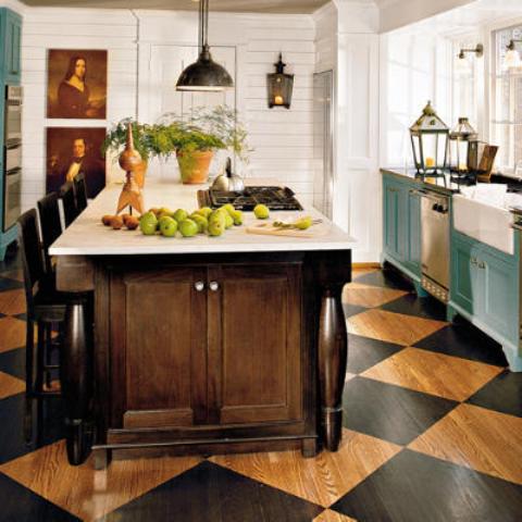 an English cottage kitchen with a checked floor, blue cabinets, a dark stained kitchen island and pretty artworks and vintage lamps