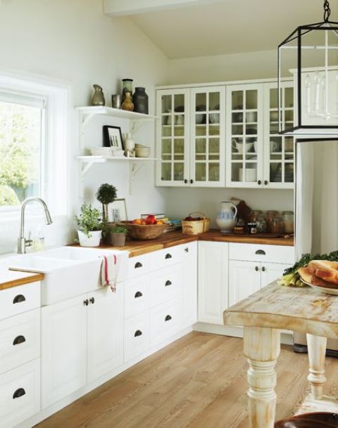 a neutral cottage kitchen with white cabinets and stained butcherblock countertops, a shabby chic table kitchen island and a vintage pendant lamp