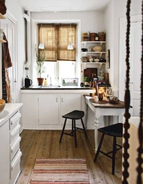 a Nordic cottage kitchen in white, with dark stained countertops, open shelves, woven shades, black stools and a striped rug