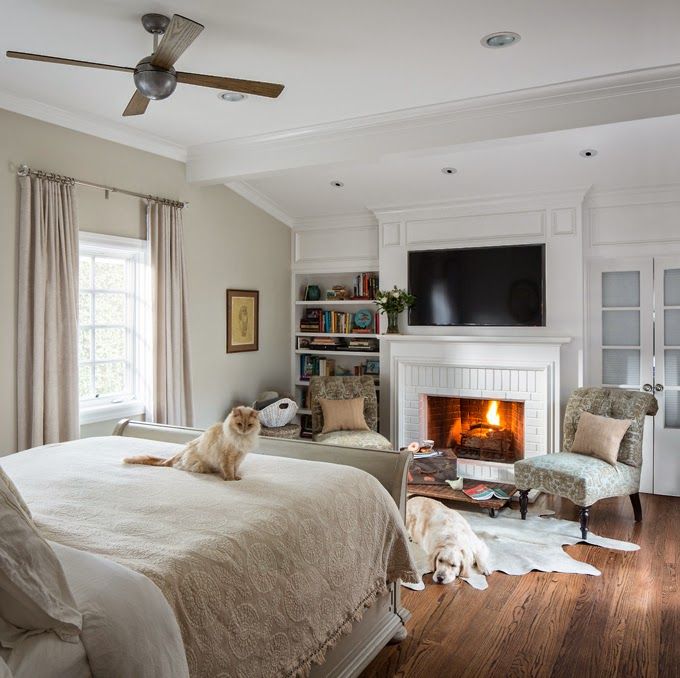 A chic neutral bedroom with a fireplace, a bed with neutral bedding, built in shelves and printed chairs is amazing