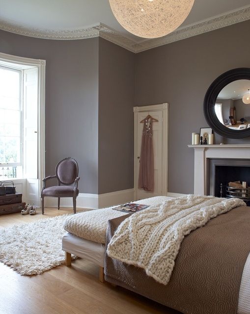 a chic bedroom with lavender walls, a fireplace, a bed with neutral bedding, a bench and a lovely vintage chair