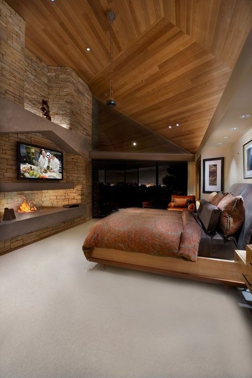 a modern chalet bedroom with an attic ceiling clad with wood, a fireplace and a TV opposite the bed with bright bedding