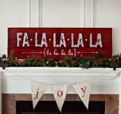 a Christmas mantel decorated with an evergreen and berry garland, with a red sign reminding of a popular Christmas song is cute and cozy