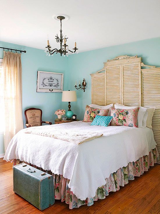 a bedroom with turquoise walls, chic vintage furniture, shutters at the headboard, a vintage chandelier and neutral and floral bedding