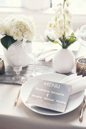 a modern white Thanksgiving tablescape with a grey runner, a black card and a dark perforated candleholder is very chic