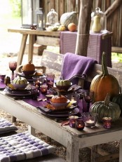 a rustic Thanksgiving tablescape with a purple table runner, napkins, glasses and candle holders, large natural pumpkins and towels