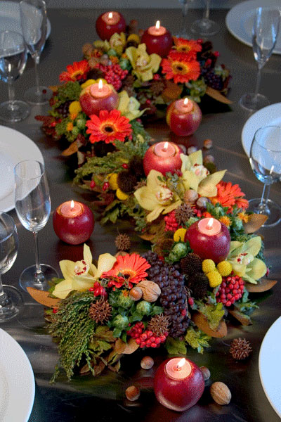 a lush Thanksgiving table runner of bold blooms, fresh berries and fruits plus candlesin apples is an amazing idea for a Thanksgiving tablescape and it looks all-natural