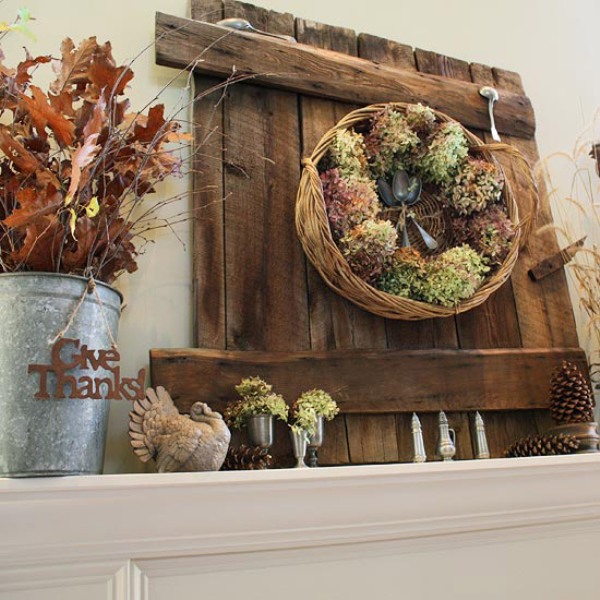 A rustic Thanksgiving mantel with dried hydrangeas, turkeys, dried leaves, twigs, pinecones and some spoons and a basket with blooms