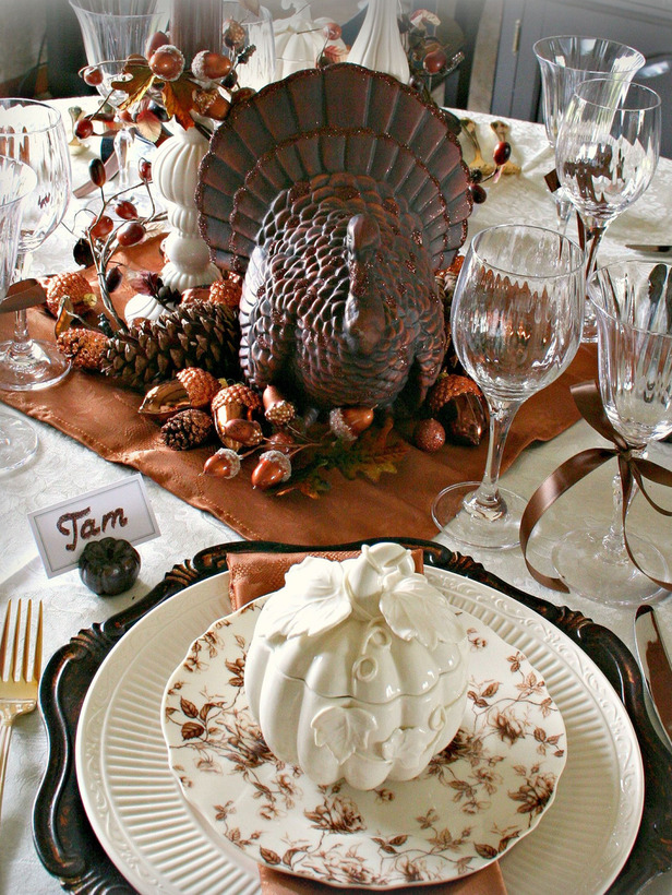 A vintage Thanksgiving tablescape with vintage chargers, a rust colored napkin and neutral linens, porcelain decor, faux acorns and nuts