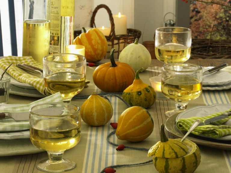A neutral and natural Thanksgiving tablescape with natural gourds and pumpkins, a green tablecloth and napkins, neutral porcelain and pillar candles