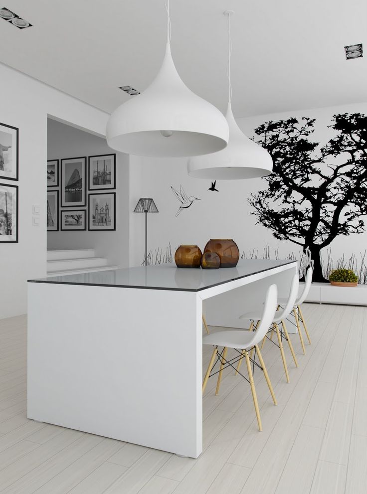 A minimalist dining space with a wall mural, a white dining table and chairs, large pendant lamps and a black and white gallery wall