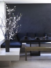 a minimal dining space with a black accent wall, a stone corner bench, blakc upholstery, a black table and a metal bench